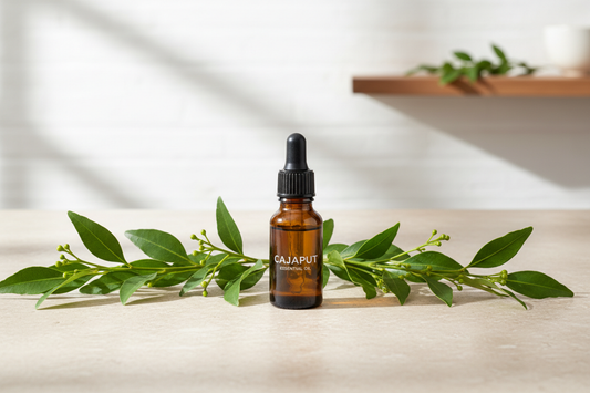 A dark amber dropper bottle nestled among fresh Melaleuca cajuputi leaves and twigs on a light stone surface