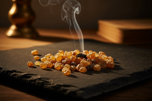Golden frankincense resin tears scattered on dark stone with warm ancient light and a wisp of smoke — the history of frankincense from ancient trade routes to modern aromatherapy