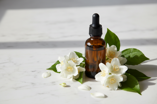 an amber glass dropper bottle on white marble surrounded by fresh white jasmine flowers