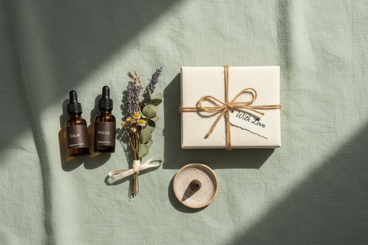 Aromatherapy gift flat lay with essential oil bottles, dried botanicals, incense holder and gift box tied with twine on sage green linen
