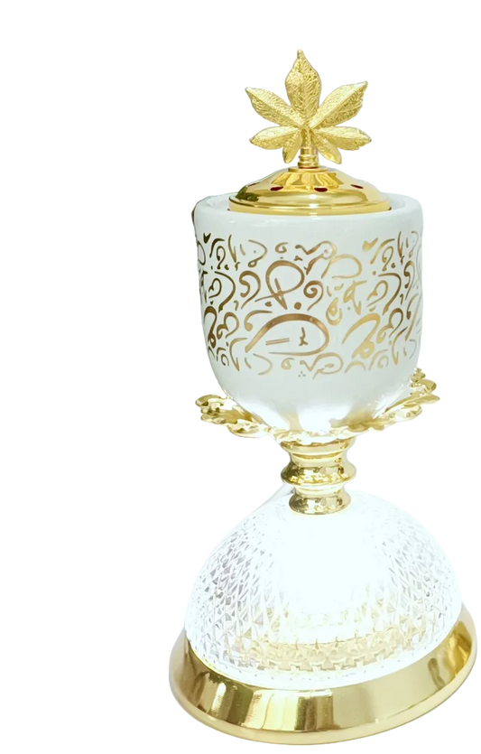 Decorative white and gold burner and lamp with intricate designs on a surface with a framed picture in the background.